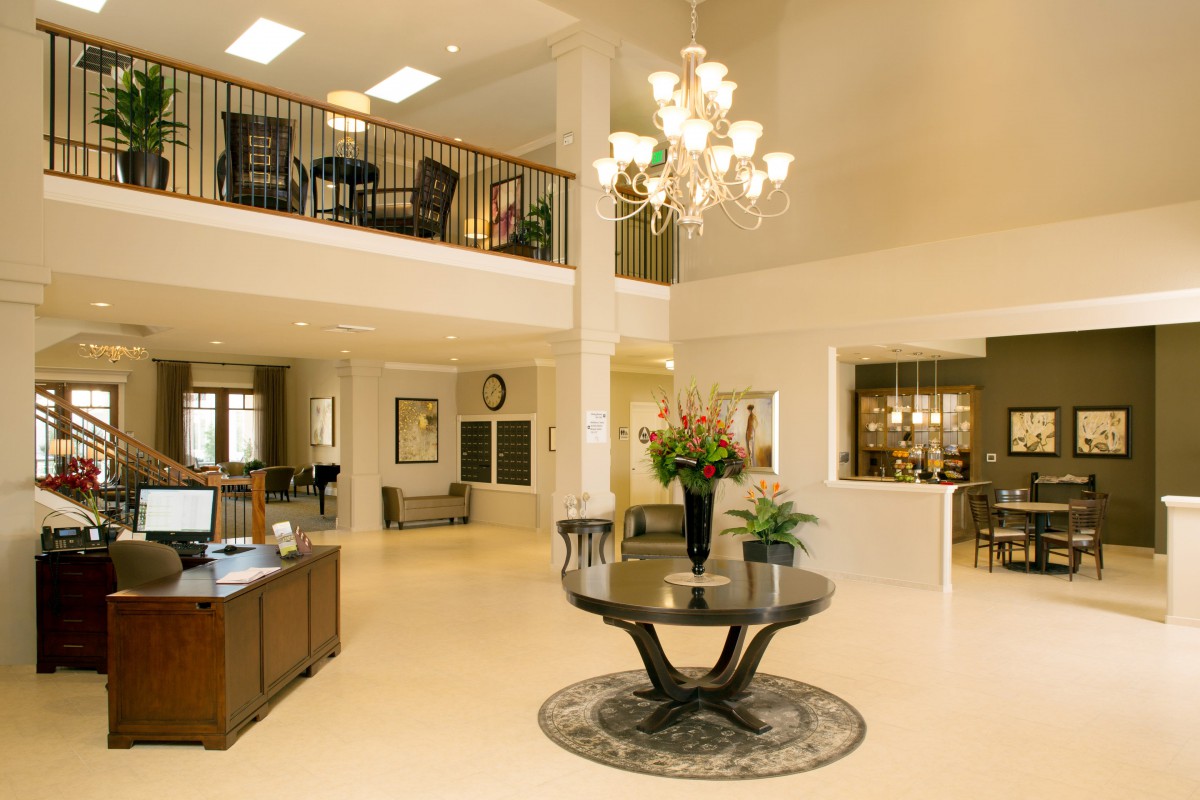 A spacious and elegant lobby with a chandelier, featuring a central table with flowers and a balcony above.