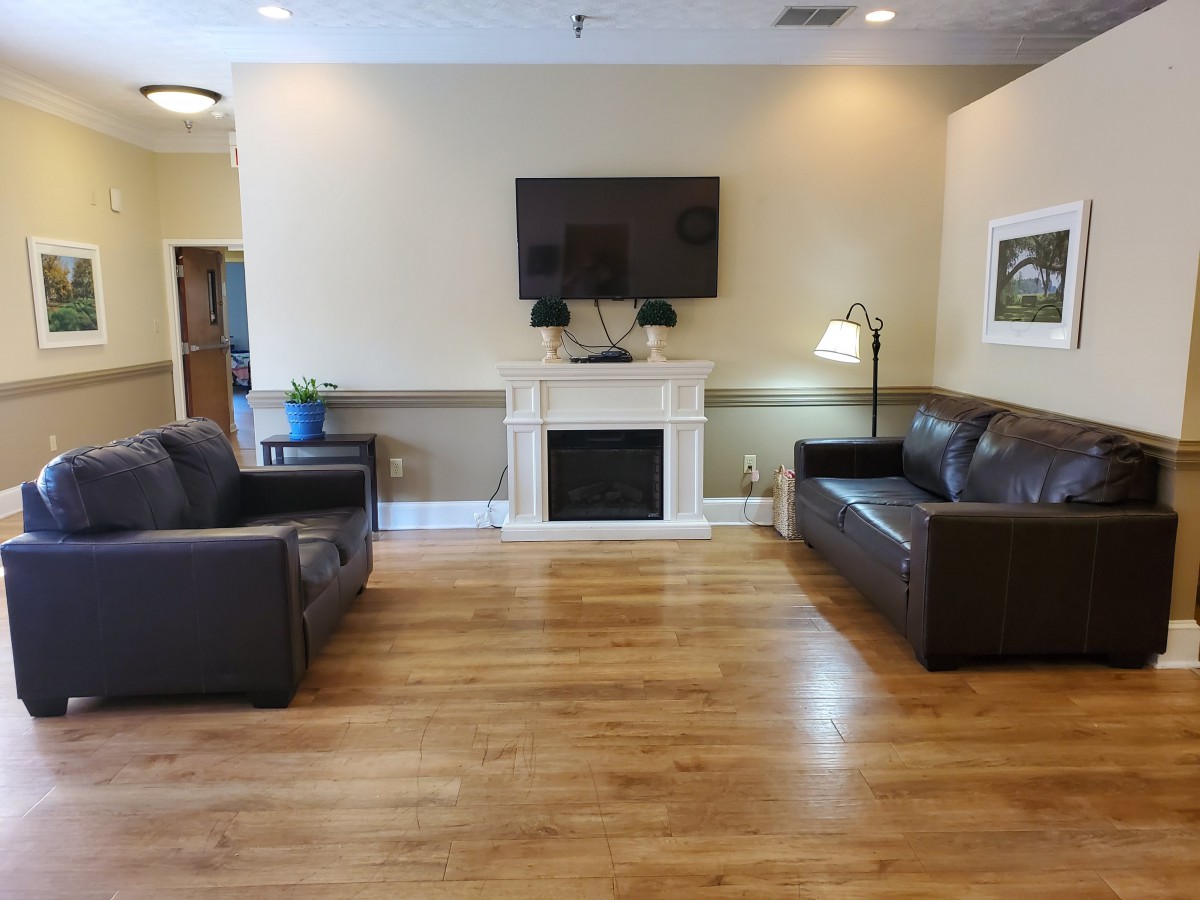 A cozy living room with two sofas, a TV mounted above a fireplace, and wooden floors.