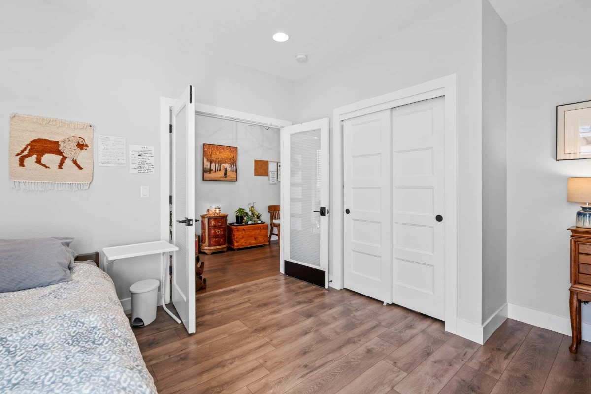 A bright interior space with double doors leading from a bedroom to a living room, featuring hardwood floors and white walls.