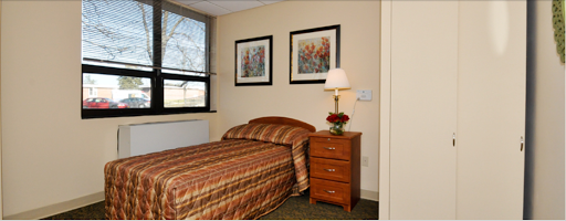 A cozy bedroom featuring a single bed, a nightstand with a lamp, and framed artwork on the walls.