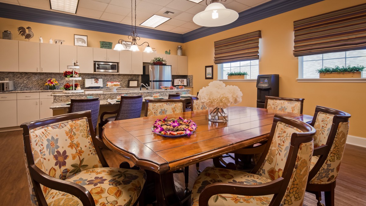 A cozy dining room with a large wooden table and elegant chairs, adjacent to a modern kitchen.