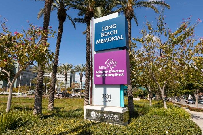 A sign for Long Beach Memorial, a medical facility, set against a background of trees and clear blue sky.