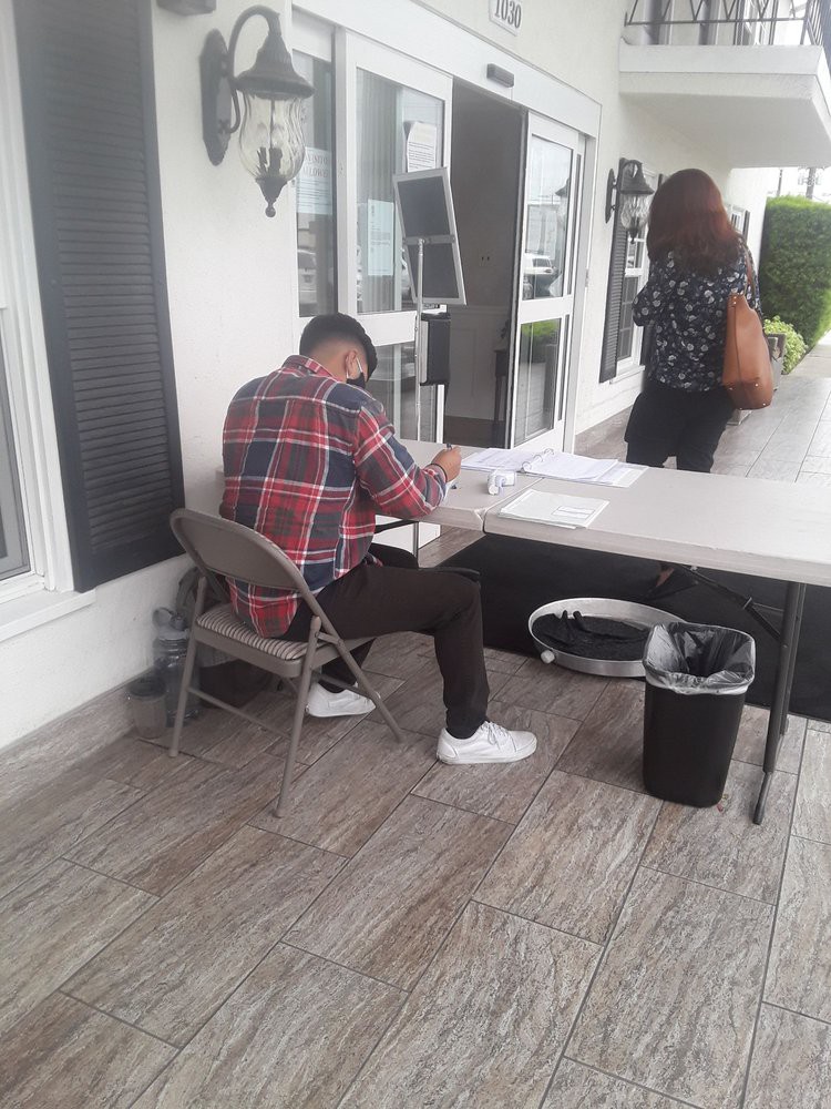 A person sits at a table outdoors, writing in a notebook.