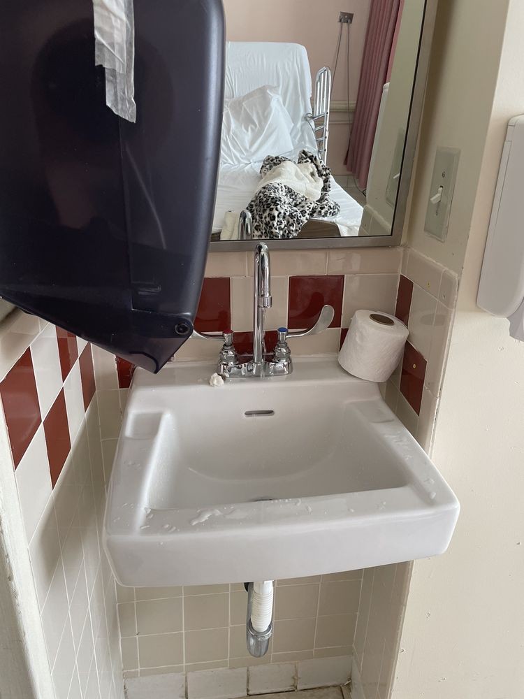 A small bathroom area with a sink, mirror, hand dryer, and toilet paper holder.