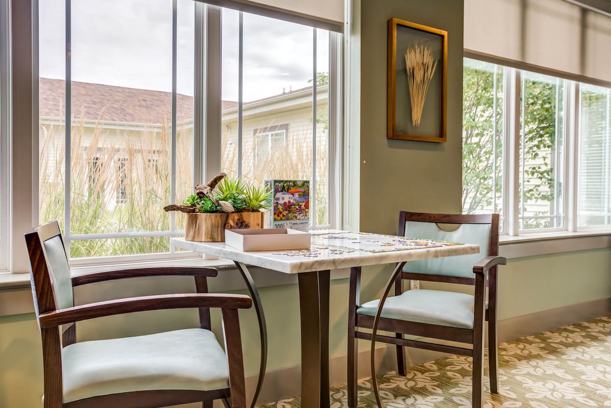 A cozy dining area with a marble table, wooden chairs, and natural light streaming through large windows.