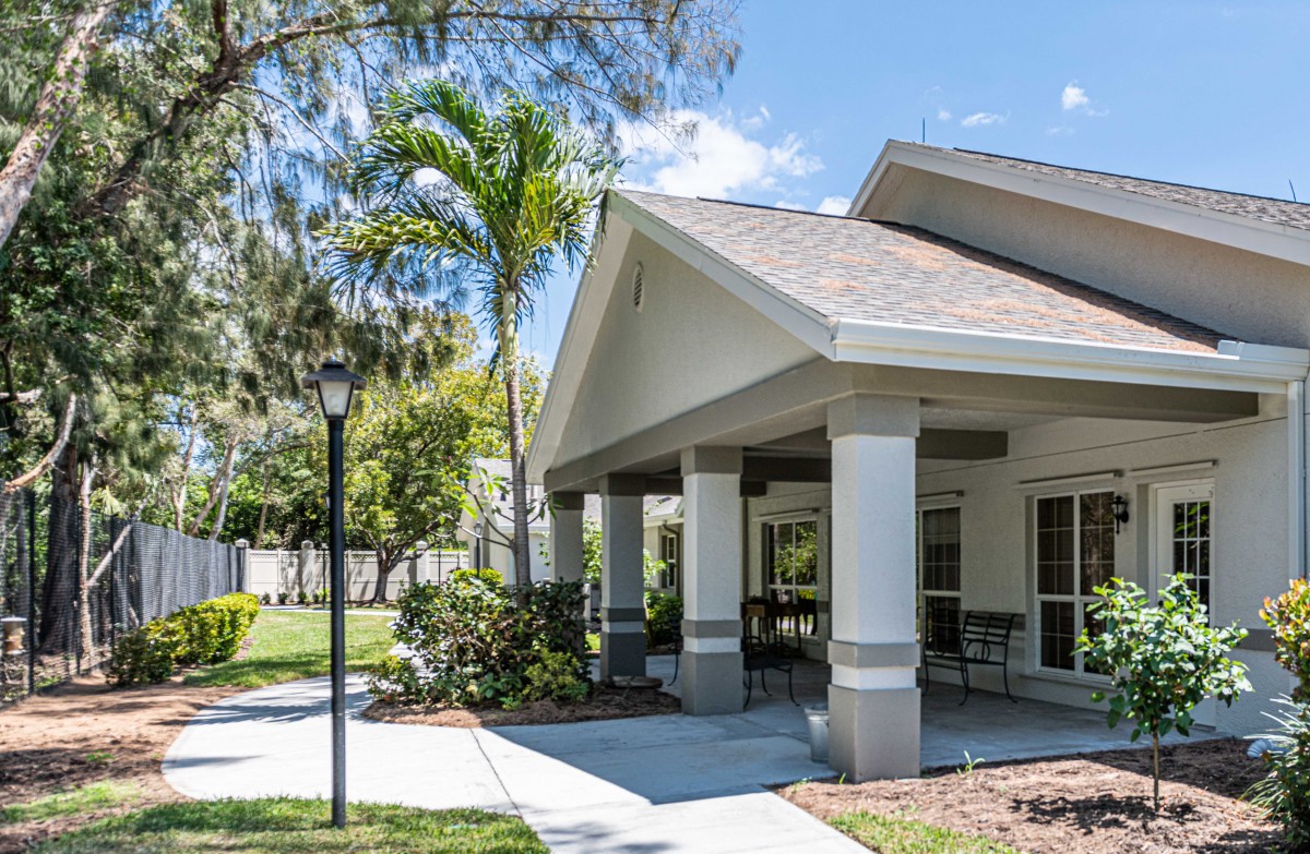 A pleasant residential house with a covered patio and surrounding palm trees on a sunny day.