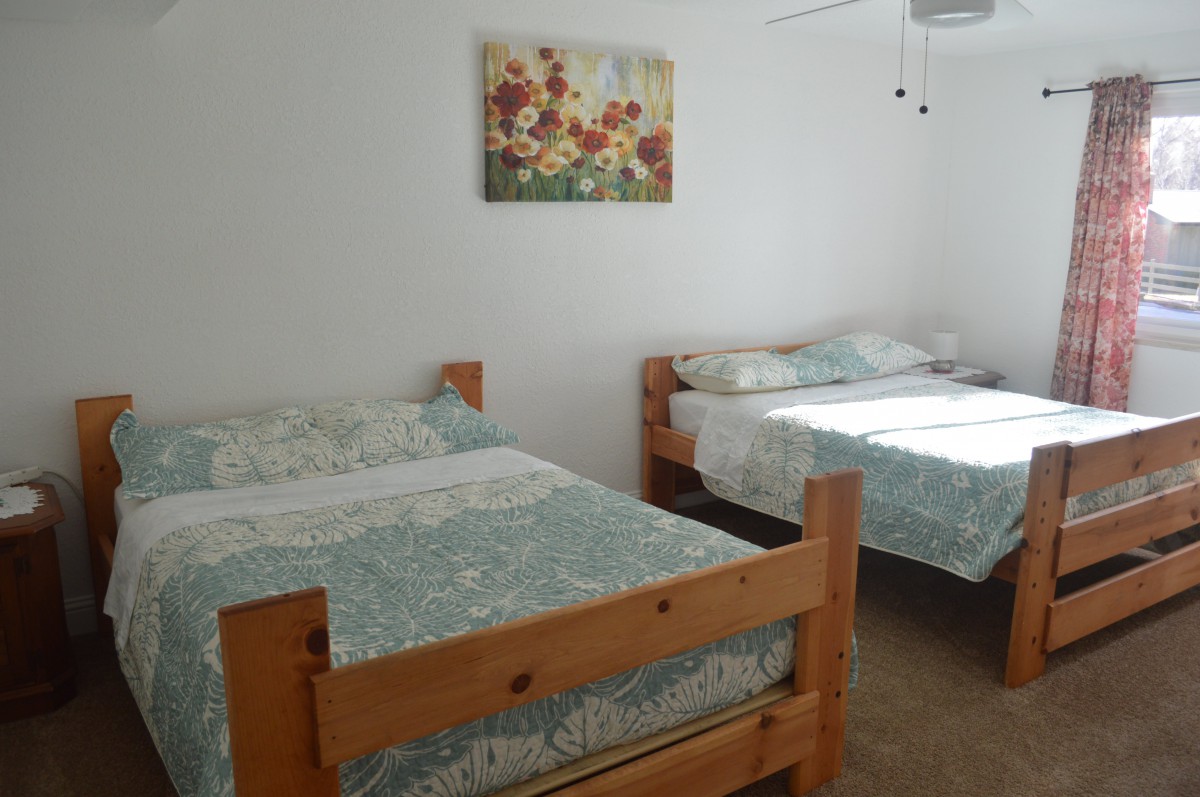A bright bedroom with two wooden beds and a floral painting on the wall.