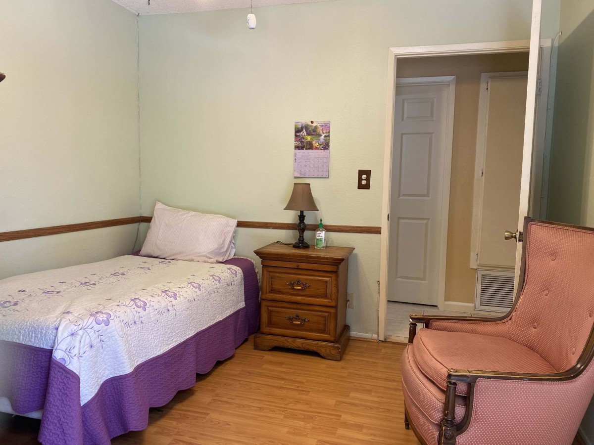 A cozy bedroom with a single bed, nightstand, and comfortable chair.