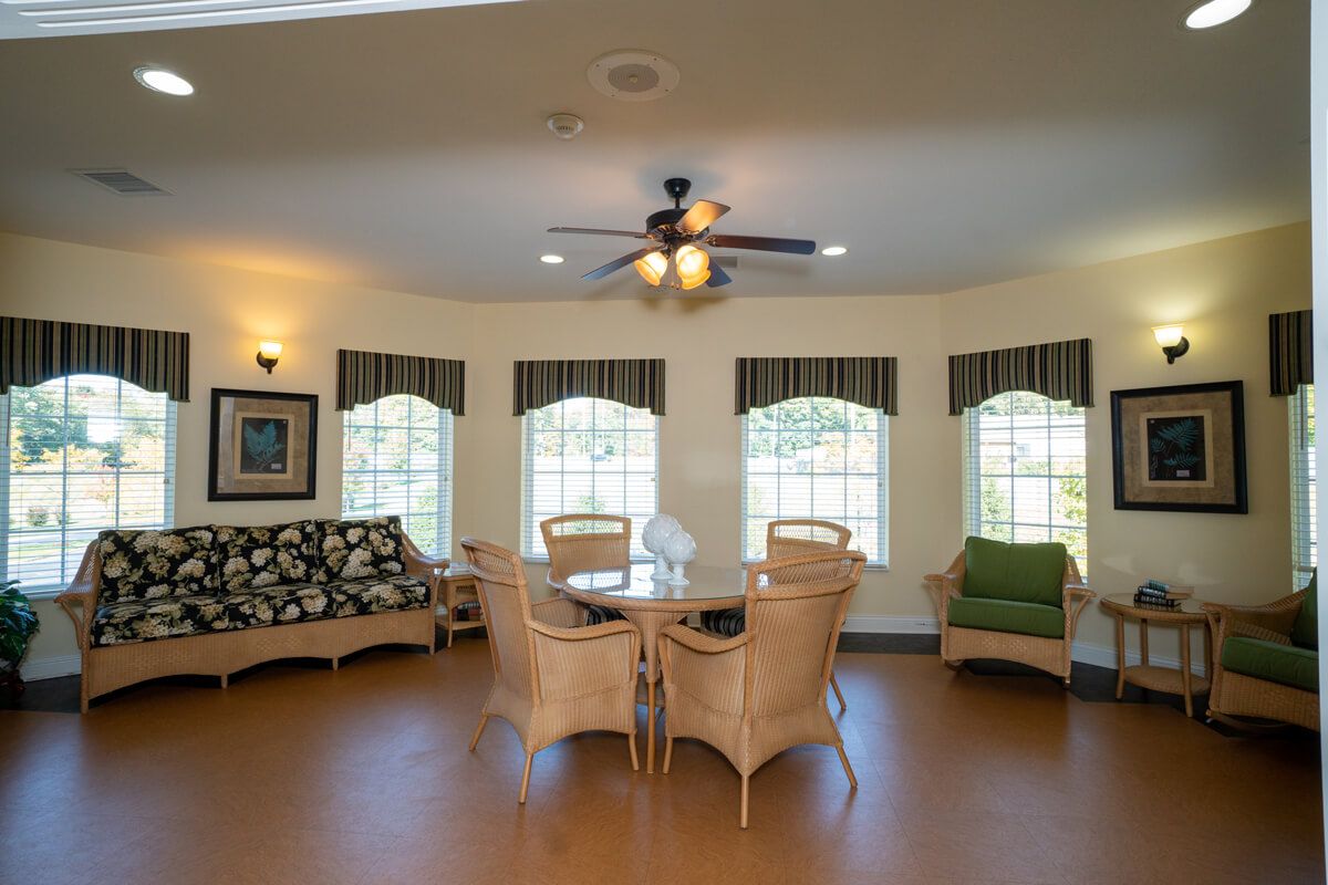 A cozy living room with wicker furniture, a ceiling fan, and large windows allowing natural light to fill the space.