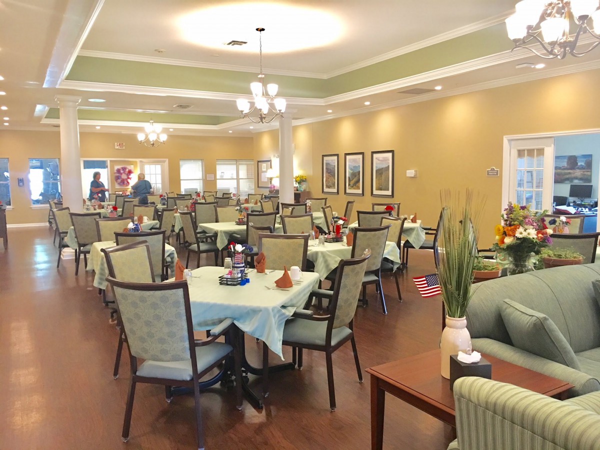A spacious dining area with neatly arranged tables and chairs, illuminated by elegant overhead lighting.
