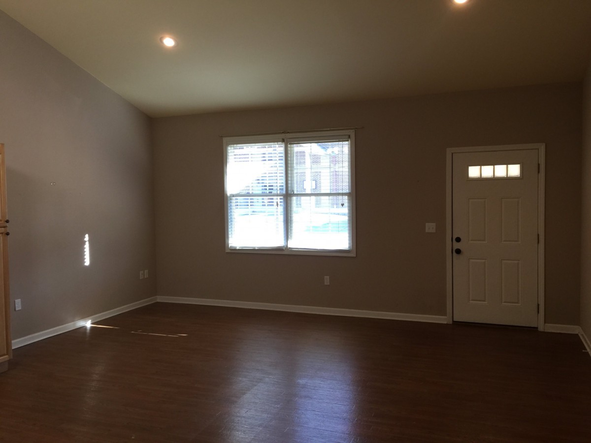 An empty room with hardwood flooring, a window, and a door.