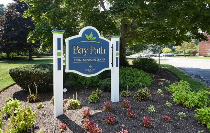 A decorative sign for Bay Path in a landscaped garden setting.