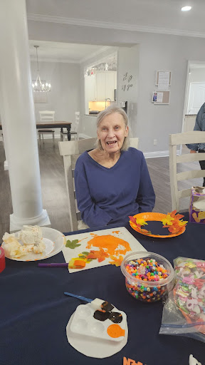 An elderly woman enjoys a creative moment at a community event, surrounded by vibrant craft supplies.