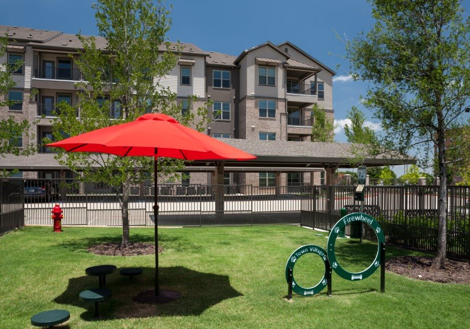 An outdoor space in an apartment complex featuring a lawn with a red umbrella and pet play equipment.