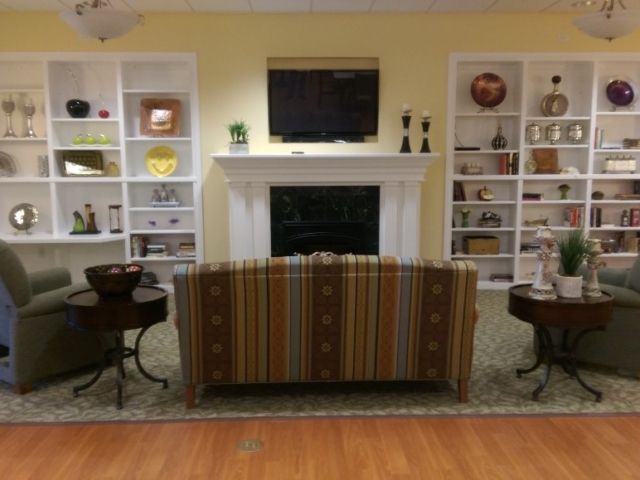 A cozy living room with a striped sofa facing a fireplace, flanked by bookshelves and a television mounted above.