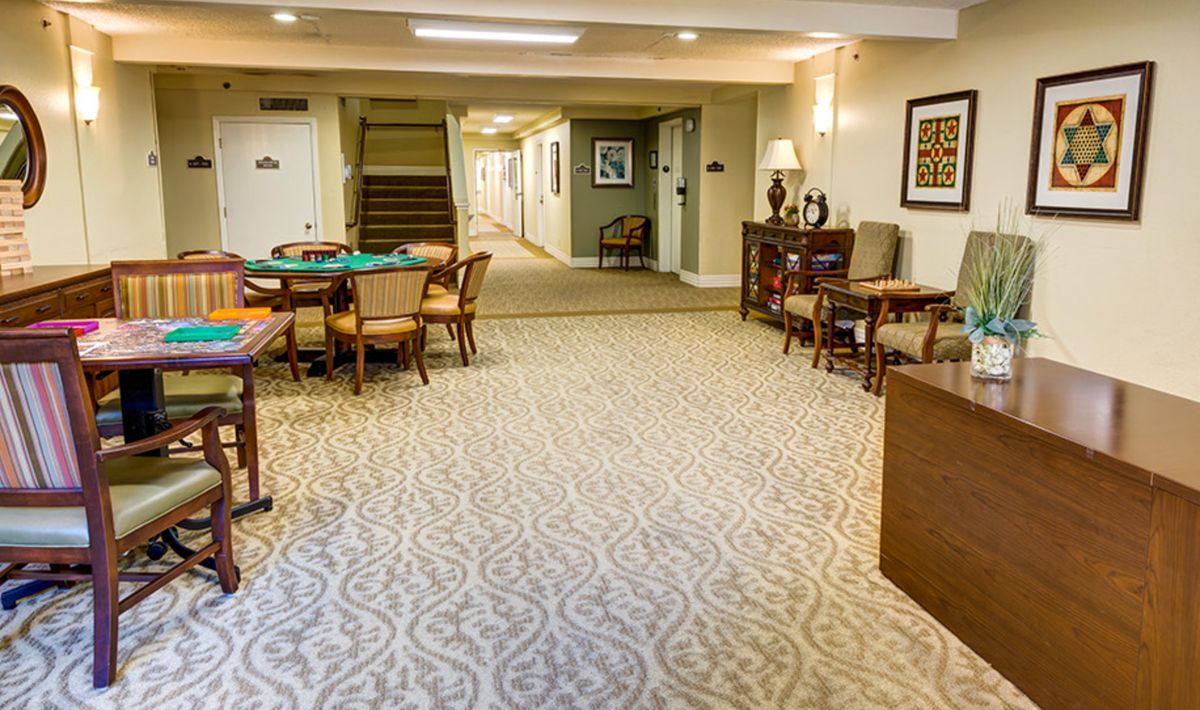 A cozy lobby area with carpeted flooring, tables, and chairs leading to a hallway.