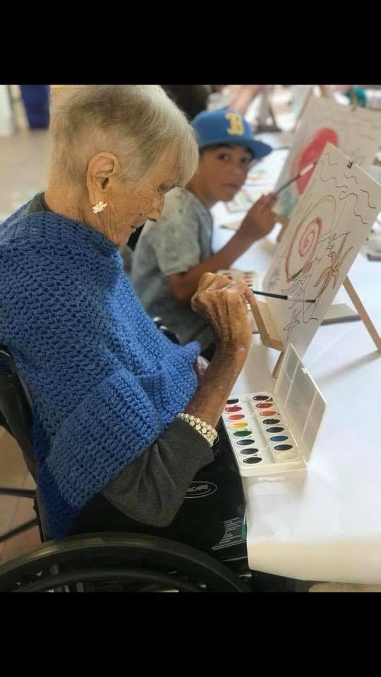 An elderly woman and a child engaged in painting together during an art class.