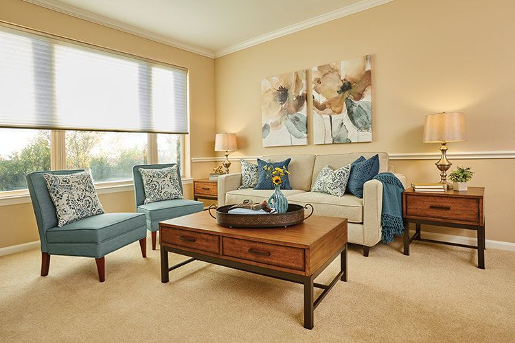 A cozy living room featuring a beige sofa with blue throw pillows, two matching armchairs, a wooden coffee table, and decorative artwork on the walls.