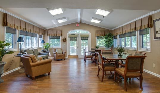 A spacious and well-lit living area with comfortable seating, tables, and ample natural light streaming through the windows.