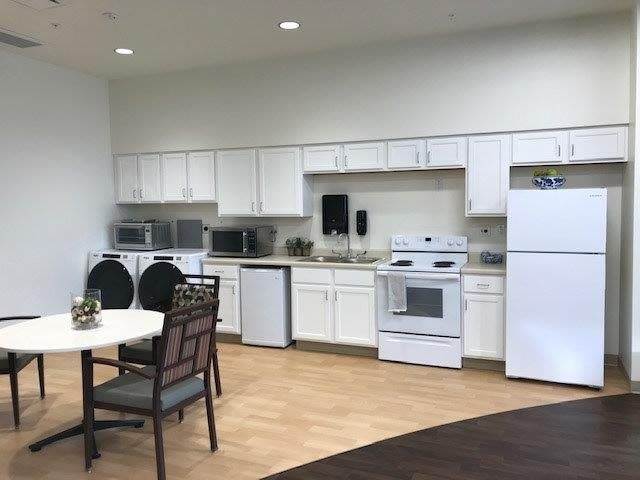 A modern kitchen with white cabinets and a dining area, featuring appliances such as a stove, refrigerator, and microwave.