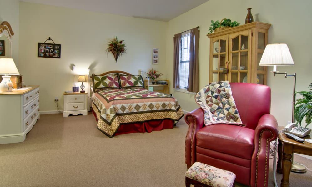A cozy bedroom with a quilt-covered bed and a red armchair.