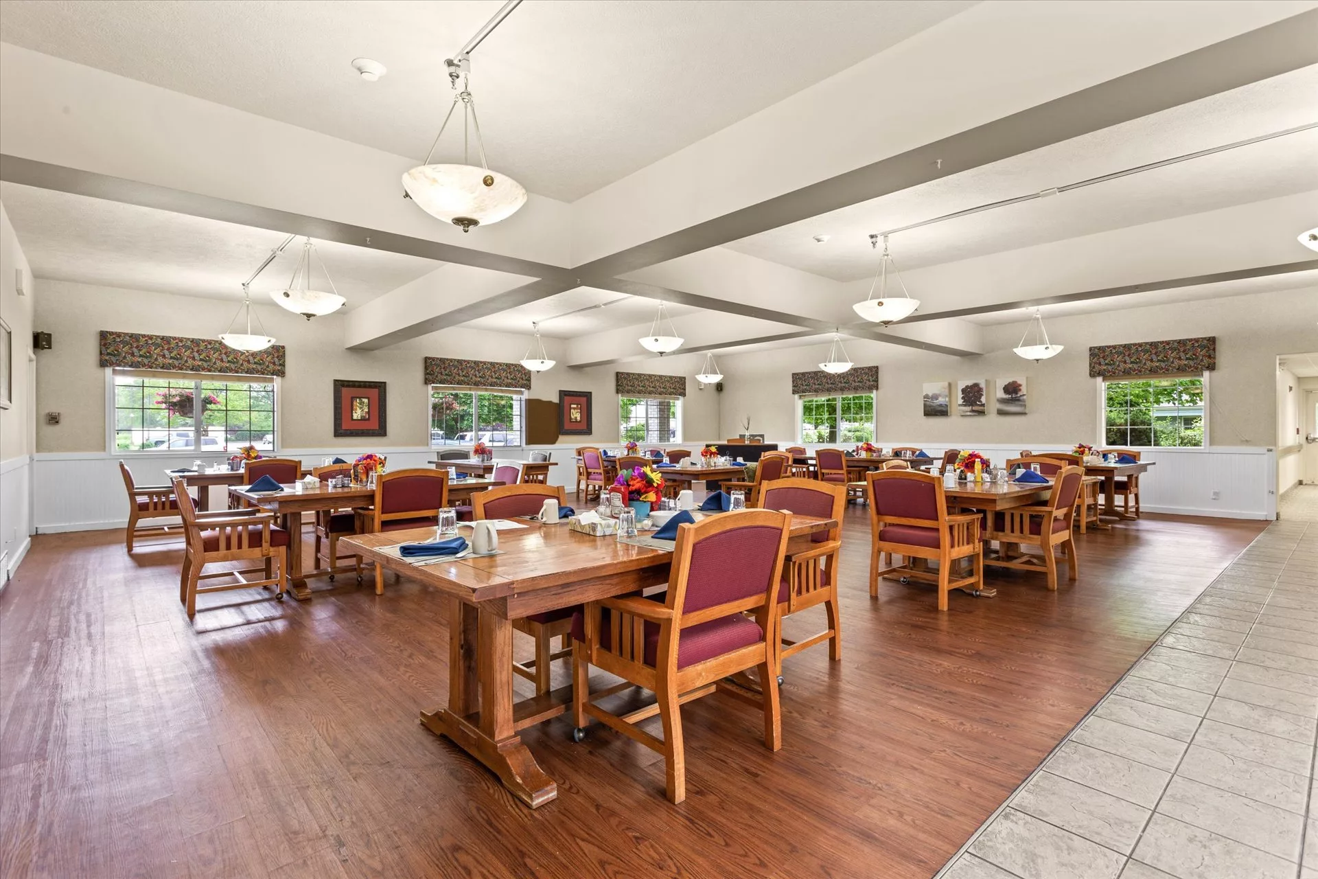 A spacious dining room with neatly arranged tables and chairs, featuring large windows and elegant lighting.