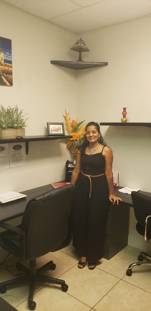 A woman stands in an office next to a desk with shelves and decorative plants.