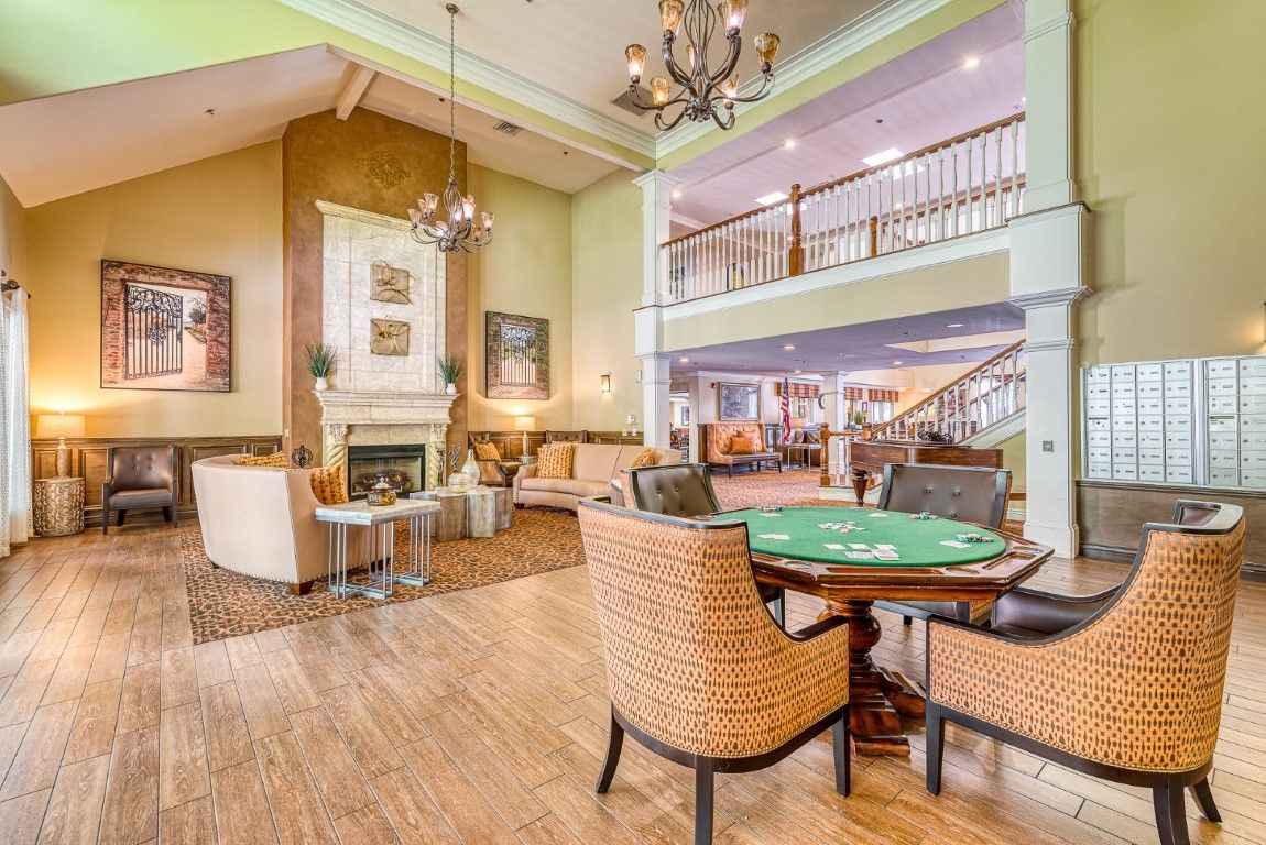 A spacious and elegantly designed living room featuring a fireplace, comfortable seating, a poker table, and a chandelier.
