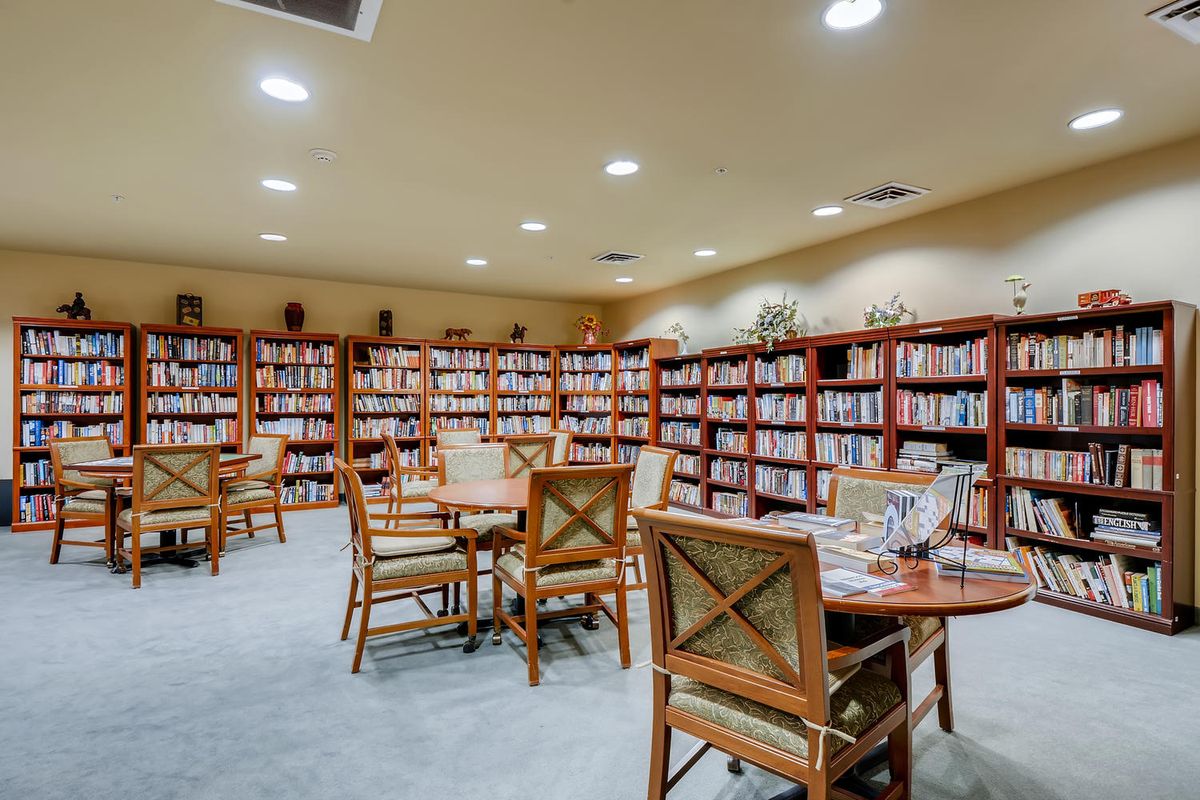A cozy library room with bookshelves, tables, and chairs.