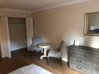 A minimalist hotel room with two chairs, a small table, and a dresser.
