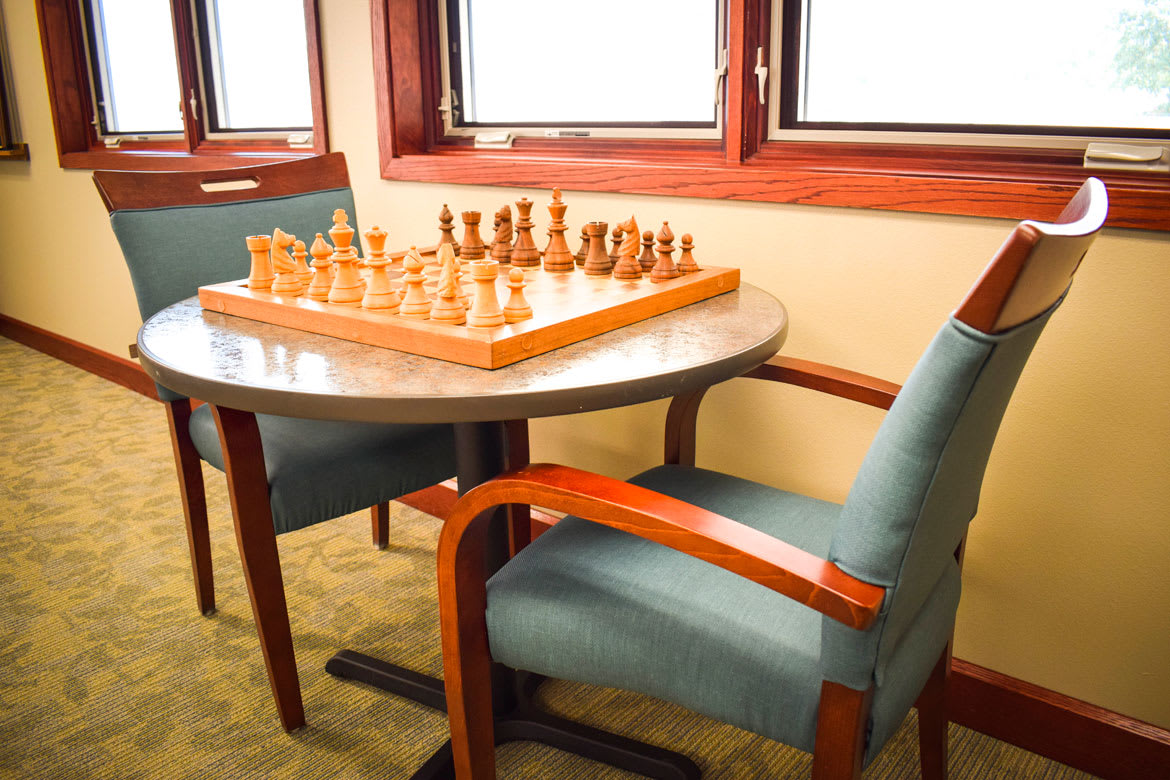 A chess set ready for play on a table with chairs in a cozy indoor setting.