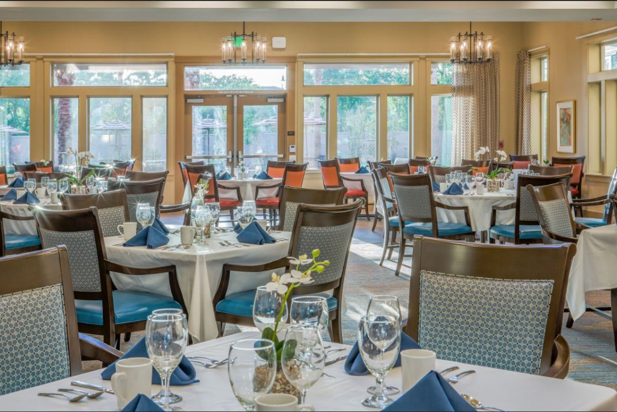 A well-decorated restaurant dining area with neatly arranged tables and chairs, featuring elegant place settings and large windows.