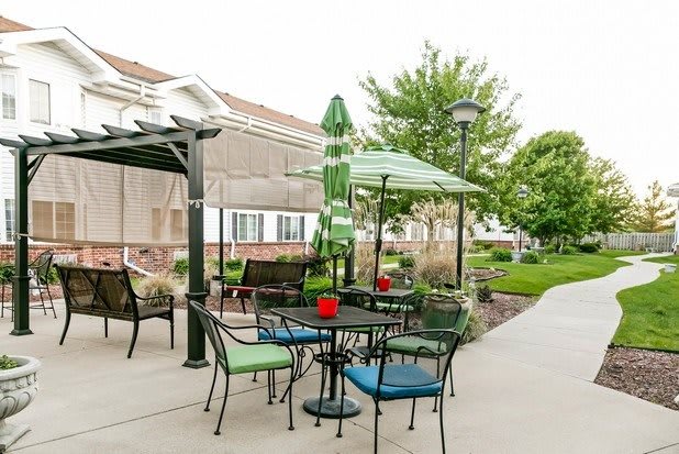 A well-maintained outdoor patio with tables, chairs, and umbrellas in a garden setting.