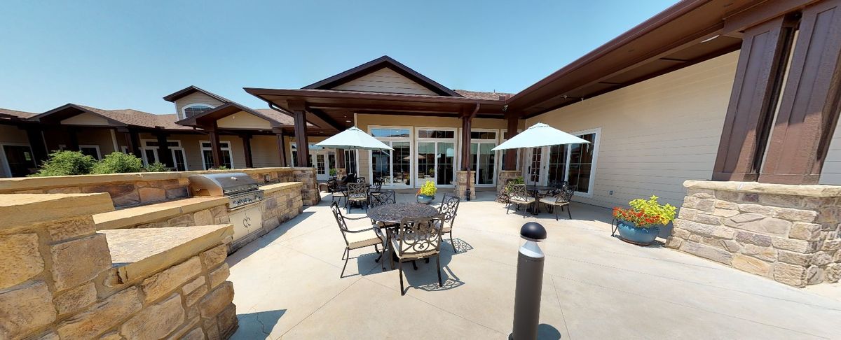 A sunny outdoor patio with tables, chairs, and umbrellas in front of a building.