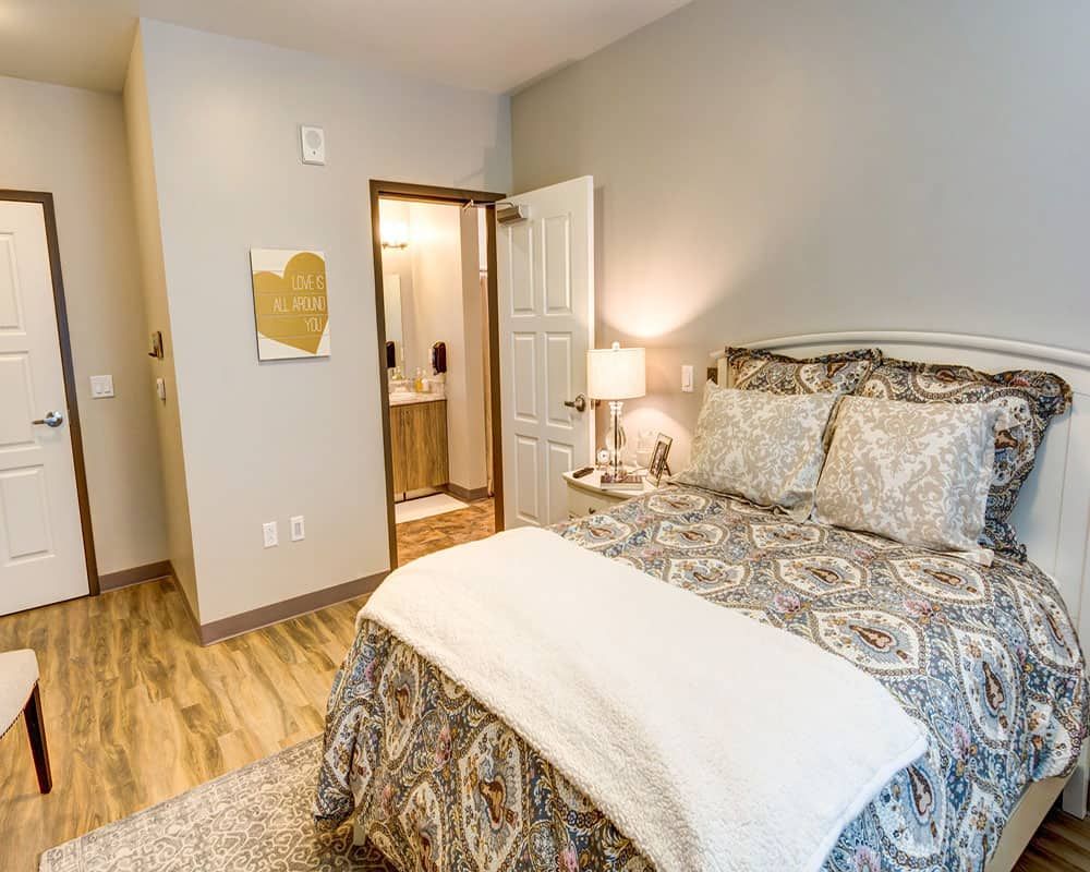 A cozy bedroom with elegant bedding, a bedside lamp, and wooden flooring.