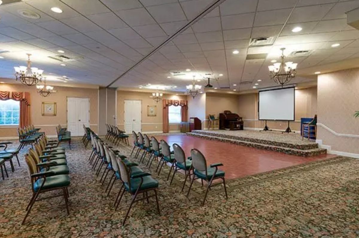 An indoor conference room setup with rows of chairs and a projector screen.