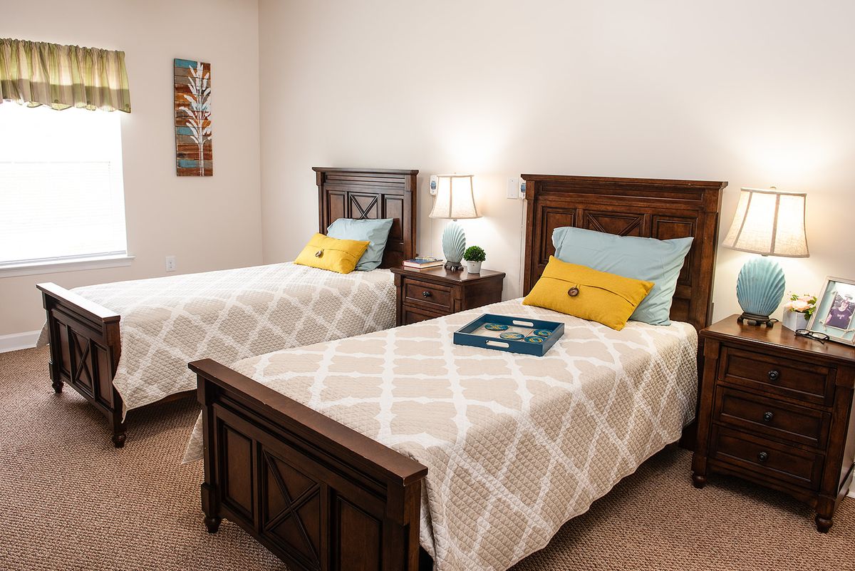 A cozy bedroom with two twin beds, featuring wooden headboards and decorative pillows, softly lit by a bedside lamp.