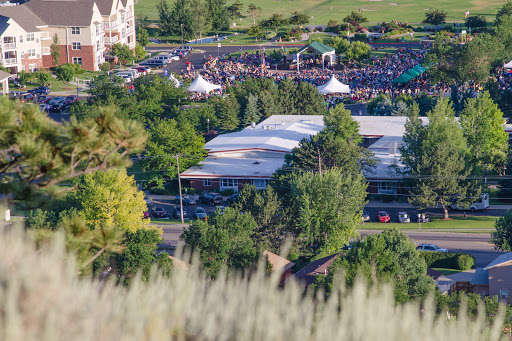 A scenic view of a large outdoor event with a gathering of people, surrounded by greenery and tents.