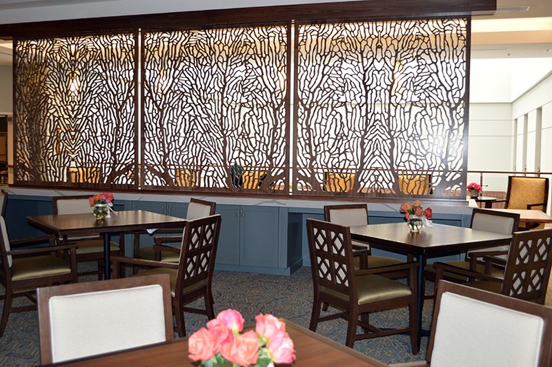 A stylish restaurant dining area featuring wooden tables and chairs, accented by a decorative screen and floral centerpieces.