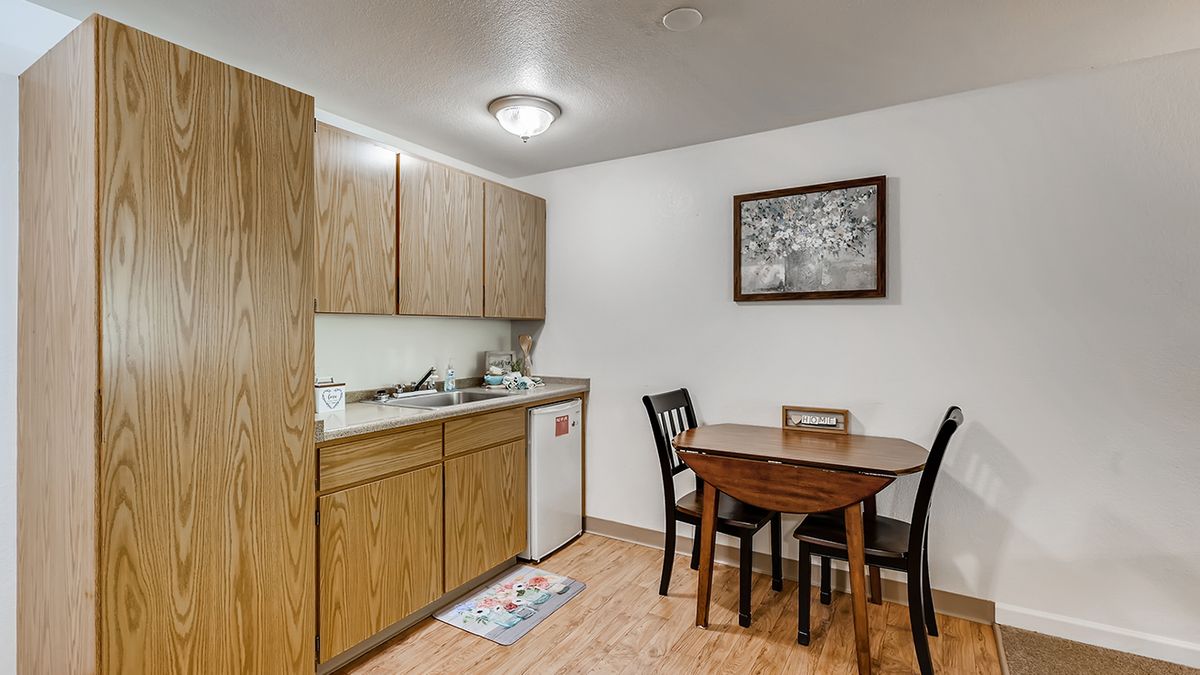 Cozy kitchen and dining area featuring wooden cabinets, a small dining table with chairs, and a decorative wall painting.