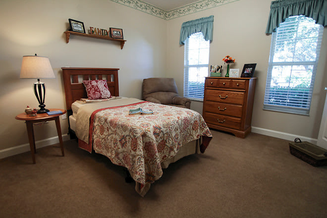 A cozy bedroom with a single bed, dresser, and armchair.