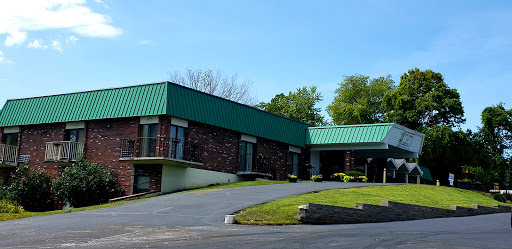A modern commercial building featuring a distinctive green roof and a brick facade, surrounded by well-maintained landscaping.