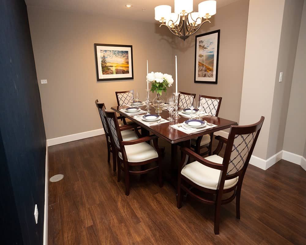 An elegantly set dining room with a wooden table, upholstered chairs, and tasteful wall art.