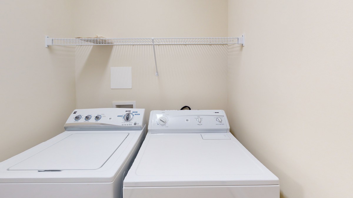 A laundry room featuring a washing machine and dryer with an overhead shelf.