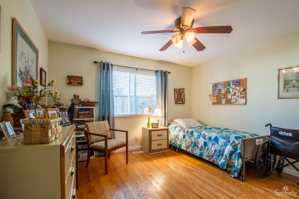 A cozy bedroom with a single bed and wooden floors, illuminated by natural light from a large window.