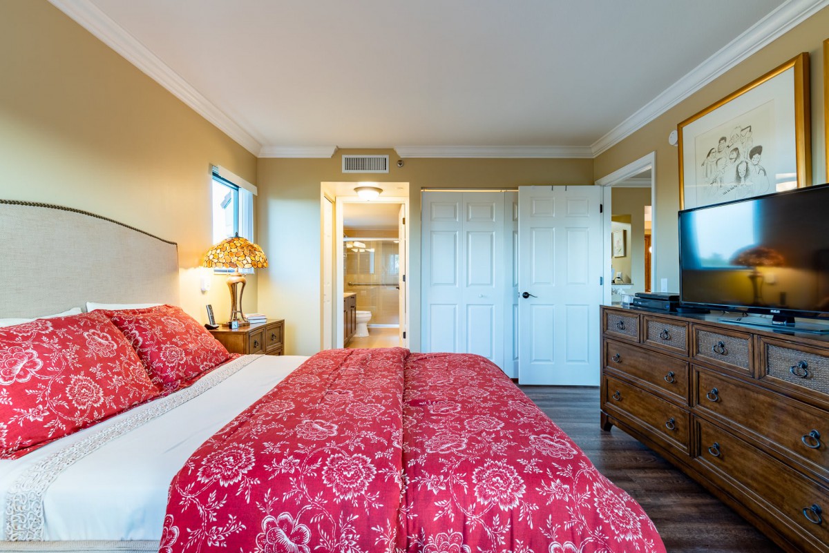 A cozy bedroom with a red comforter, a bedside lamp, and wooden furniture.