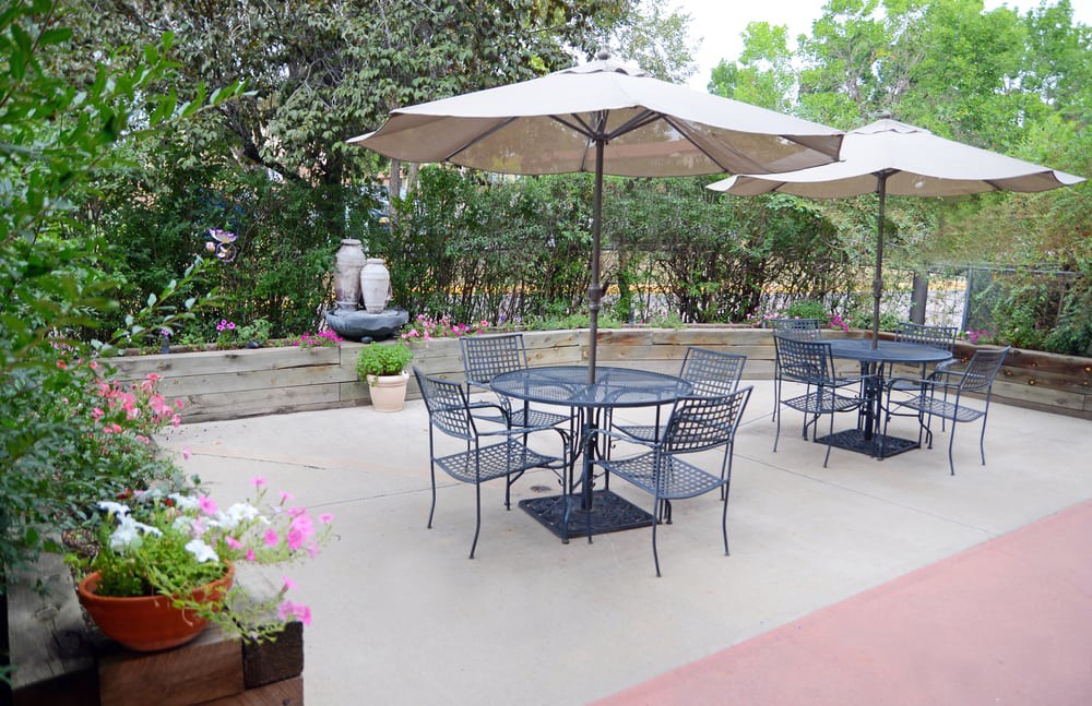 A serene patio with tables and chairs under umbrellas surrounded by lush greenery and flowers.