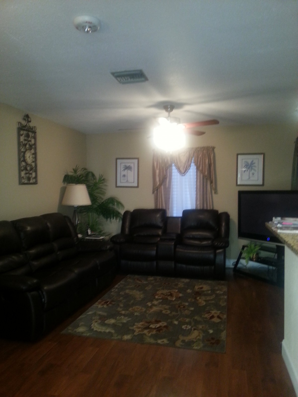 A cozy living room with leather sofas, a carpet, and a ceiling fan.