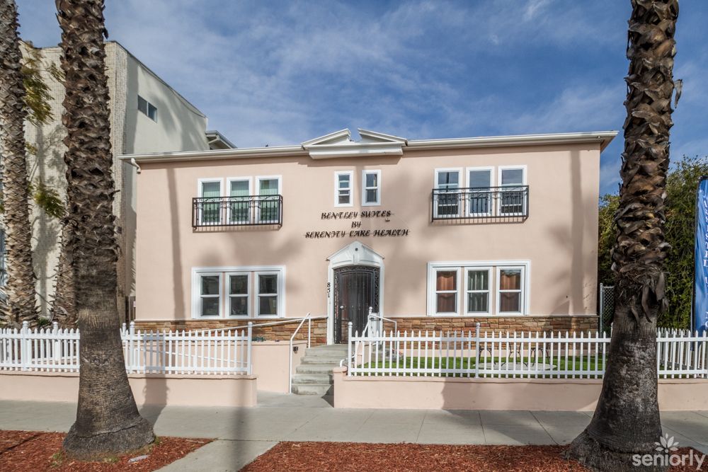 A two-story residential building with a stucco exterior and a small front yard behind a white fence.