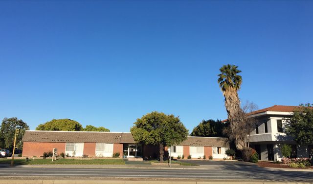 A suburban residential building with a palm tree under a clear blue sky.